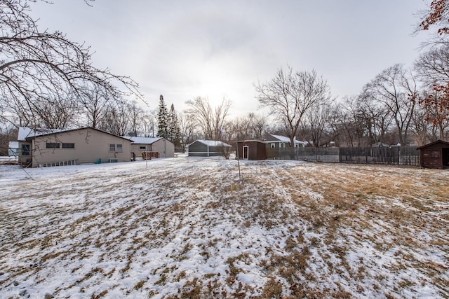 snowy yard featuring a detached garage, fence, and an outbuilding