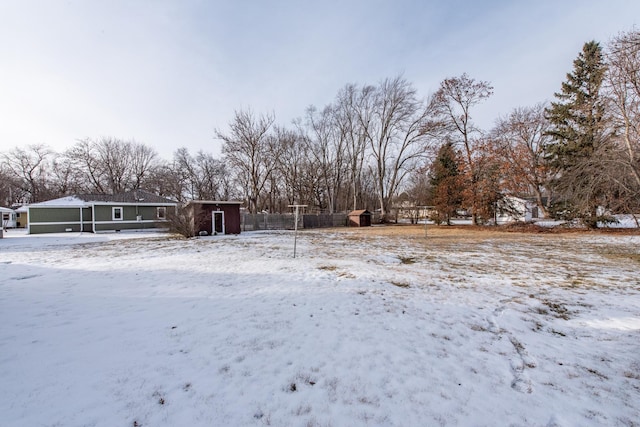 yard covered in snow featuring a storage shed, an outdoor structure, fence, and a garage