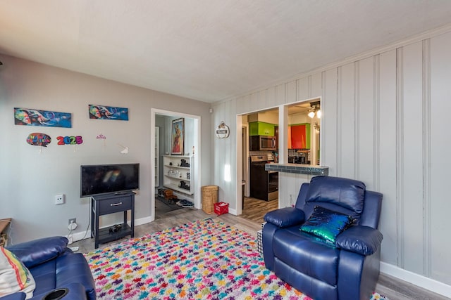 living room with a ceiling fan, baseboards, and wood finished floors