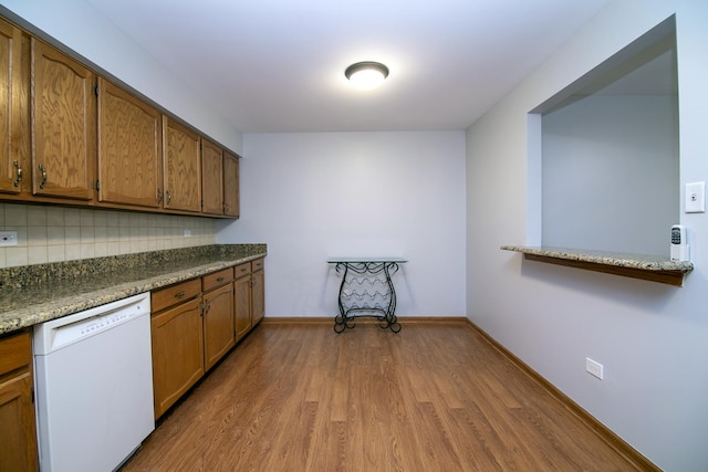 kitchen with baseboards, brown cabinetry, wood finished floors, white dishwasher, and backsplash