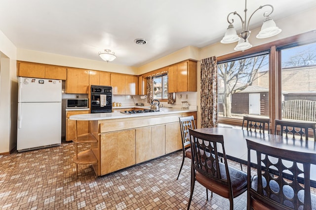 kitchen featuring a peninsula, visible vents, light countertops, and freestanding refrigerator