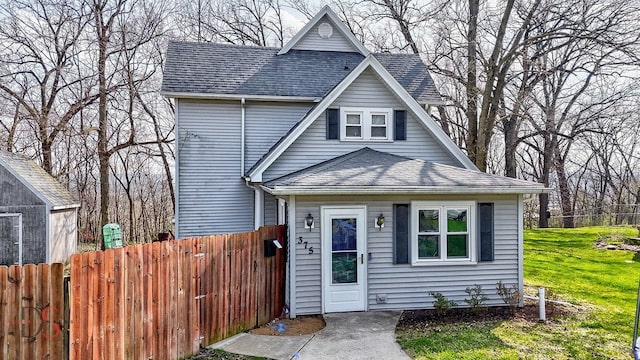 view of front of property with fence, a shingled roof, and a front lawn