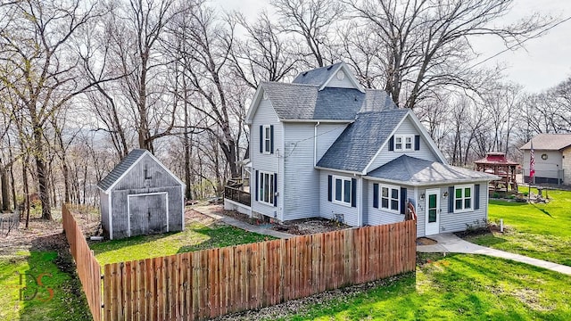 rear view of house with an outdoor structure, fence, roof with shingles, a yard, and a storage shed