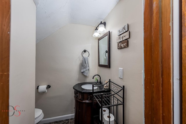 half bath with vanity, baseboards, vaulted ceiling, and toilet