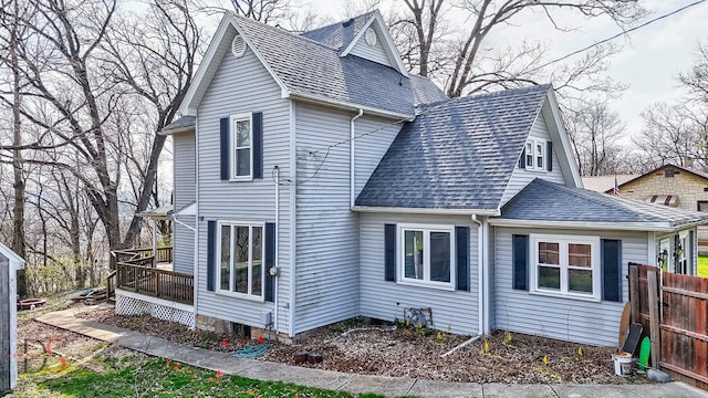 view of side of property featuring roof with shingles, fence, and a deck