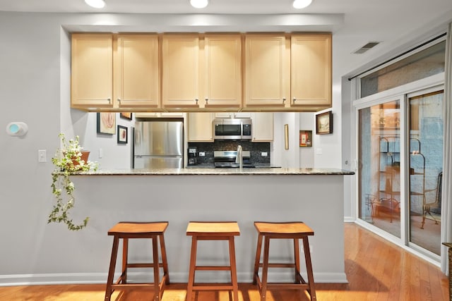 kitchen featuring a peninsula, a breakfast bar, light wood-style floors, appliances with stainless steel finishes, and tasteful backsplash