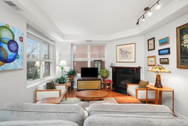 living room with wood finished floors, a fireplace with flush hearth, visible vents, baseboards, and a tray ceiling