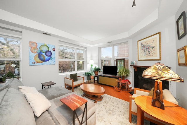 living room with a tray ceiling, wood finished floors, a high end fireplace, and visible vents