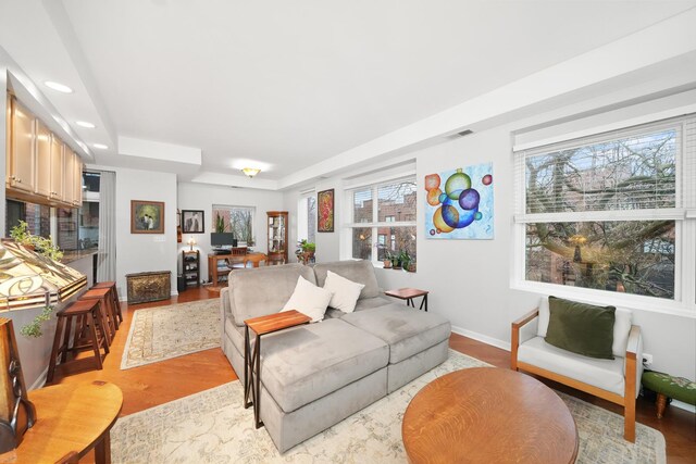 living room with light wood finished floors, baseboards, a tray ceiling, and recessed lighting