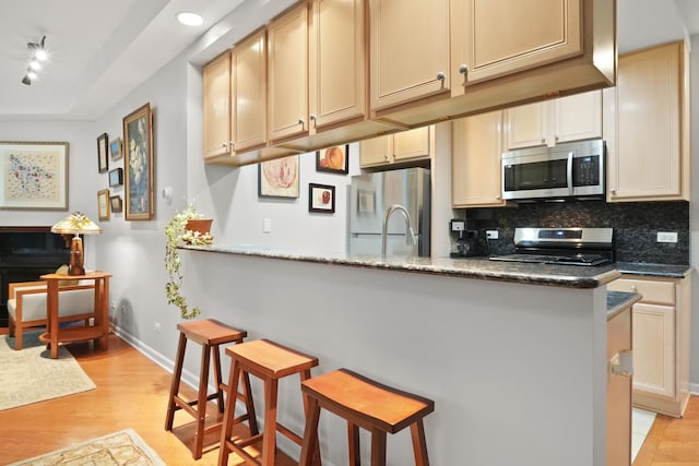 kitchen featuring appliances with stainless steel finishes, a breakfast bar, light wood-style flooring, and tasteful backsplash