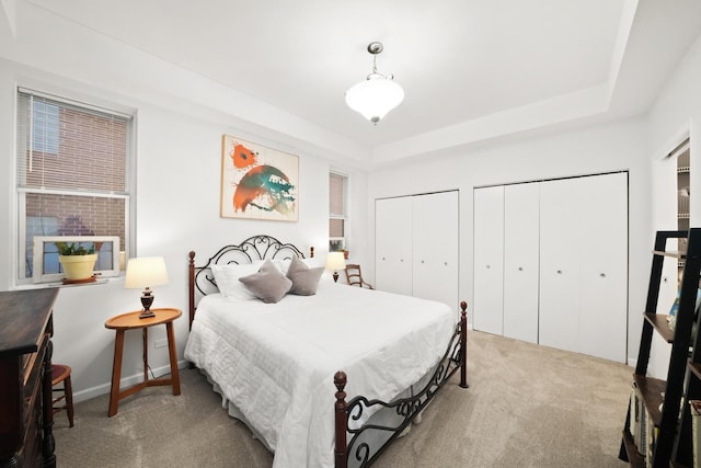 carpeted bedroom featuring baseboards, a raised ceiling, and multiple closets