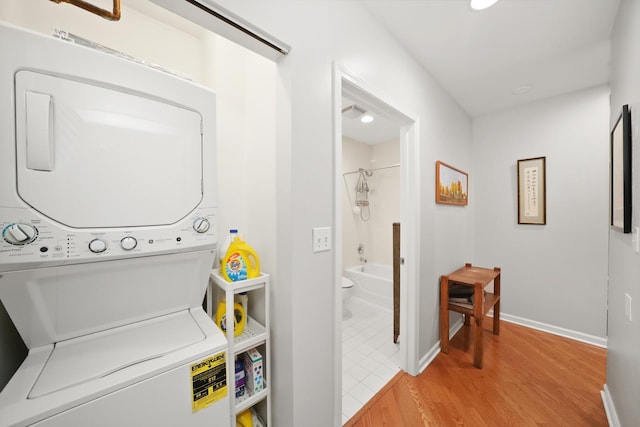 clothes washing area featuring stacked washer and dryer, laundry area, light wood-style floors, and baseboards