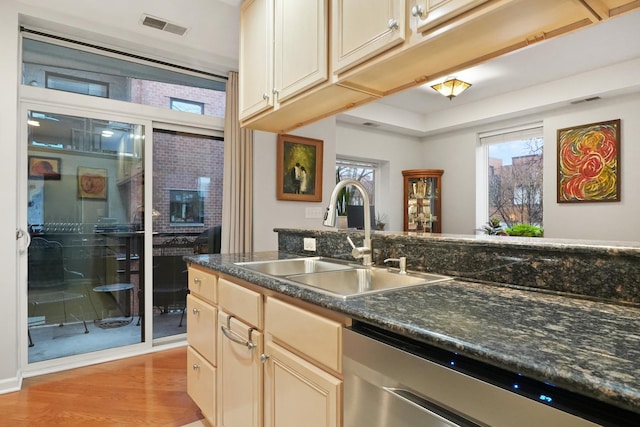 kitchen with a sink, visible vents, dishwasher, light wood finished floors, and dark countertops