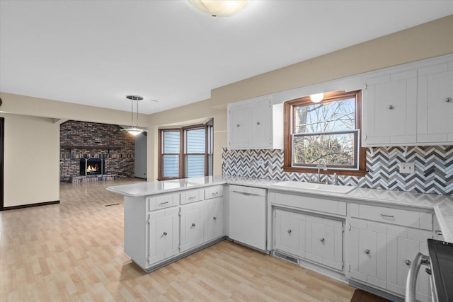 kitchen featuring a sink, a peninsula, light countertops, a brick fireplace, and dishwasher