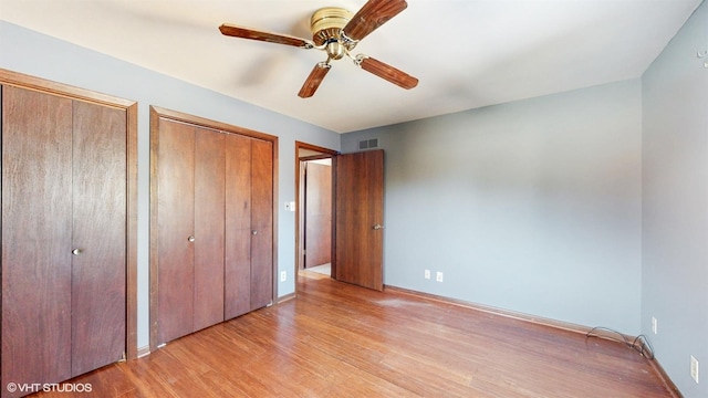 unfurnished bedroom featuring multiple closets, light wood-type flooring, visible vents, and a ceiling fan