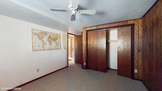 unfurnished bedroom featuring wooden walls, baseboards, a ceiling fan, carpet, and a closet