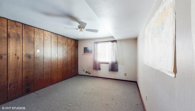 unfurnished room featuring ceiling fan, carpet, and wooden walls