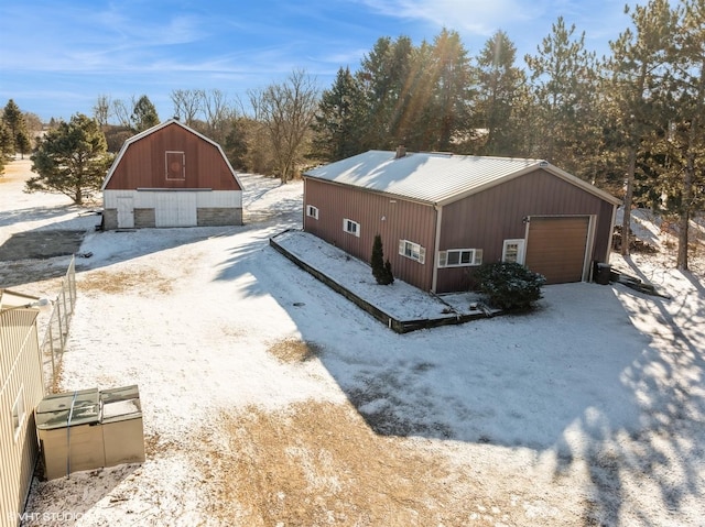 view of snow covered exterior featuring a barn, driveway, a detached garage, metal roof, and an outdoor structure