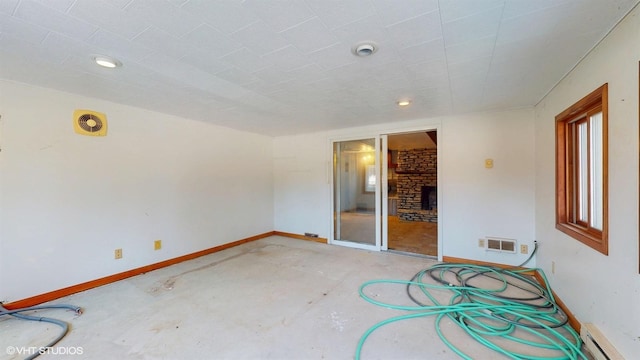 unfurnished room featuring a baseboard heating unit, visible vents, a fireplace, and baseboards