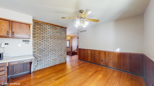 spare room featuring a ceiling fan, a wainscoted wall, visible vents, and light wood finished floors