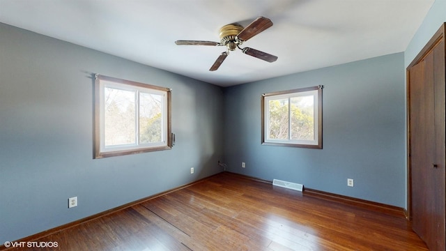 empty room featuring plenty of natural light, visible vents, wood-type flooring, and baseboards