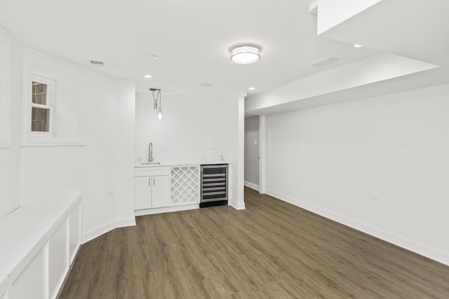 interior space featuring beverage cooler, baseboards, dark wood-style flooring, wet bar, and a sink