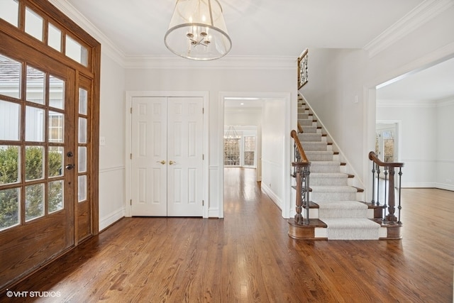 entryway featuring crown molding, stairs, a chandelier, and wood finished floors