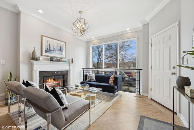 living room with a glass covered fireplace, crown molding, light wood finished floors, baseboards, and a chandelier