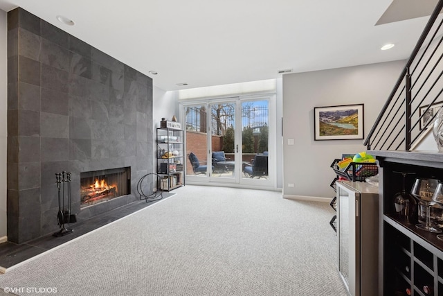 carpeted living room with visible vents, baseboards, a tiled fireplace, stairs, and recessed lighting