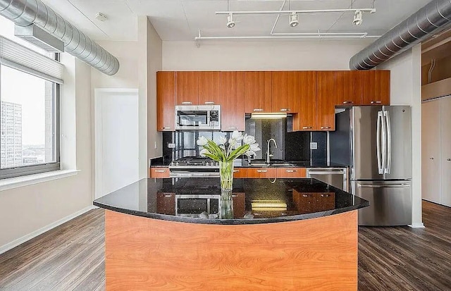 kitchen with stainless steel appliances, dark wood-style flooring, brown cabinets, and tasteful backsplash