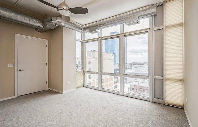 carpeted spare room featuring visible vents, floor to ceiling windows, baseboards, and a ceiling fan