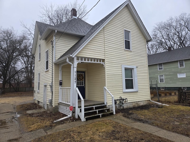 view of front of home with covered porch, a chimney, fence, and roof with shingles