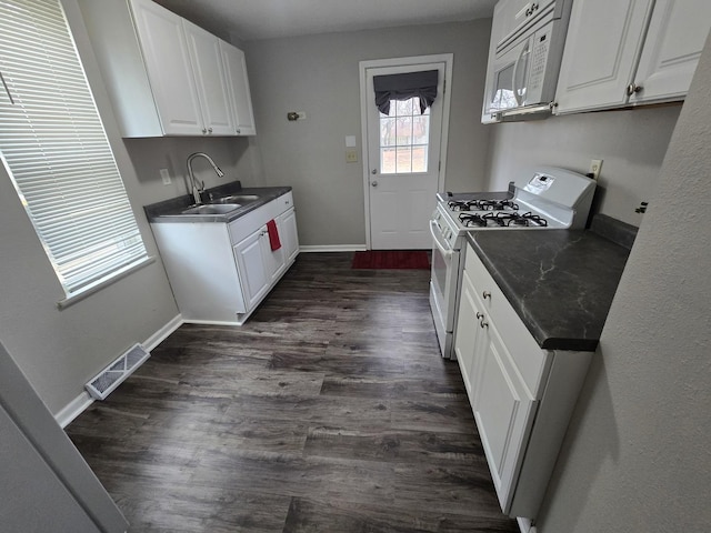 kitchen with white appliances, dark countertops, a sink, and visible vents