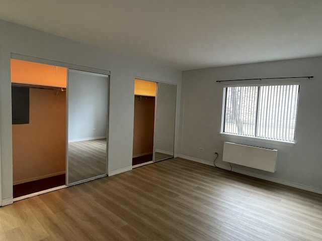 unfurnished bedroom featuring baseboards, radiator heating unit, wood finished floors, and multiple closets