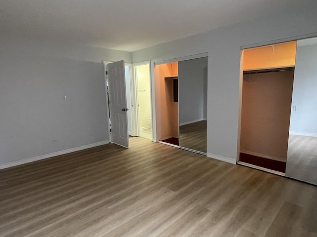 unfurnished bedroom with wood finished floors, two closets, and baseboards