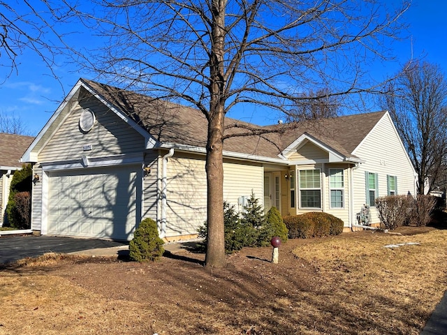 ranch-style house with an attached garage, a shingled roof, and aphalt driveway