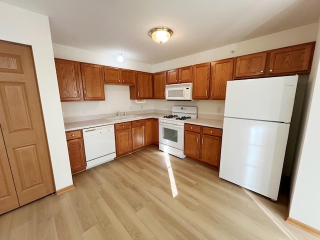 kitchen featuring white appliances, brown cabinets, light countertops, light wood-type flooring, and a sink