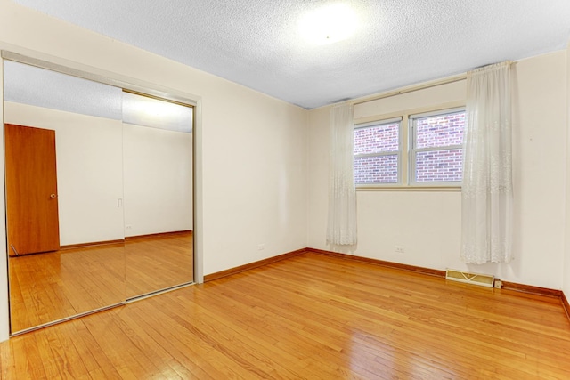 unfurnished bedroom with visible vents, baseboards, a closet, a textured ceiling, and wood-type flooring