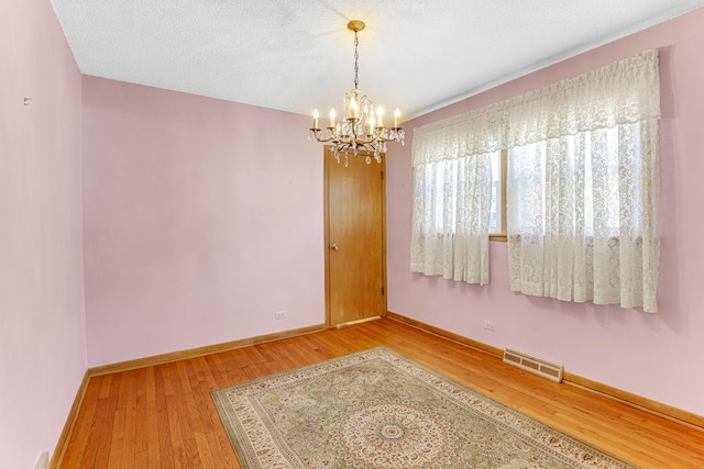 spare room with light wood-type flooring, visible vents, a textured ceiling, an inviting chandelier, and baseboards