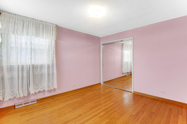 unfurnished bedroom with visible vents, multiple windows, a textured ceiling, and hardwood / wood-style flooring