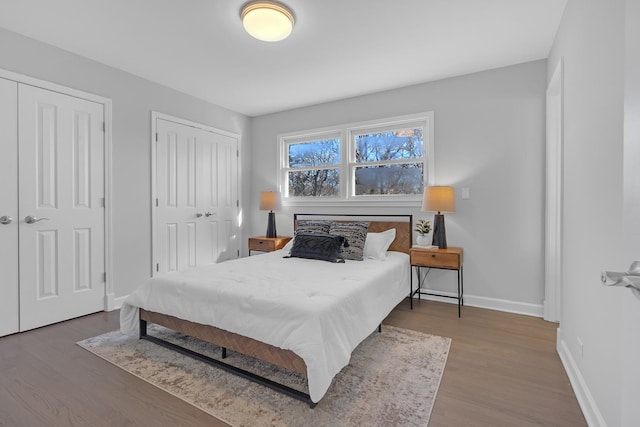 bedroom with wood finished floors, two closets, and baseboards