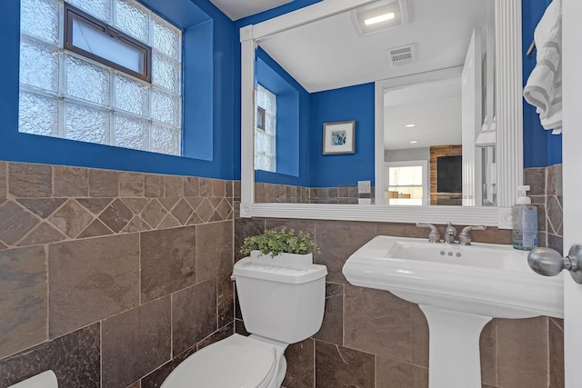 bathroom featuring visible vents, tile walls, toilet, a wainscoted wall, and a sink