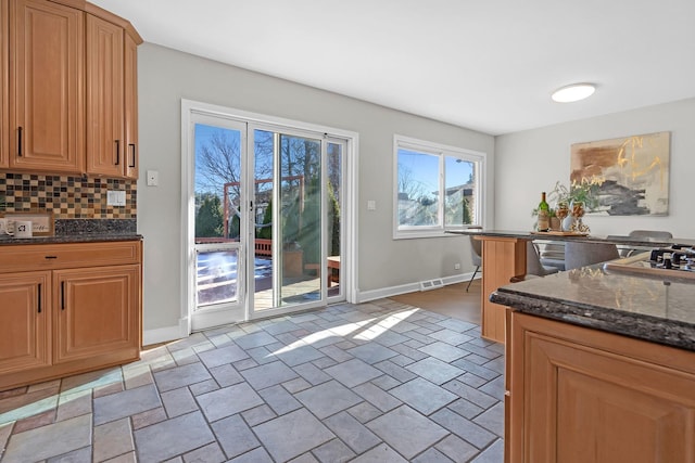 kitchen featuring stone finish flooring, baseboards, decorative backsplash, and dark stone counters