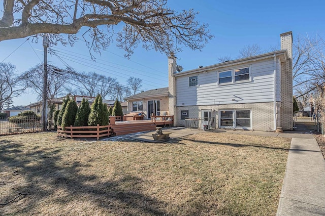 back of house with brick siding, a chimney, a lawn, fence, and a deck