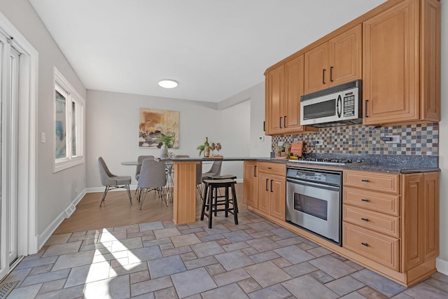 kitchen featuring stainless steel appliances, a breakfast bar, baseboards, and tasteful backsplash