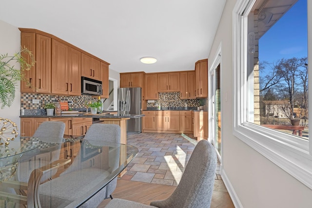 kitchen featuring tasteful backsplash, baseboards, dark countertops, appliances with stainless steel finishes, and stone finish flooring