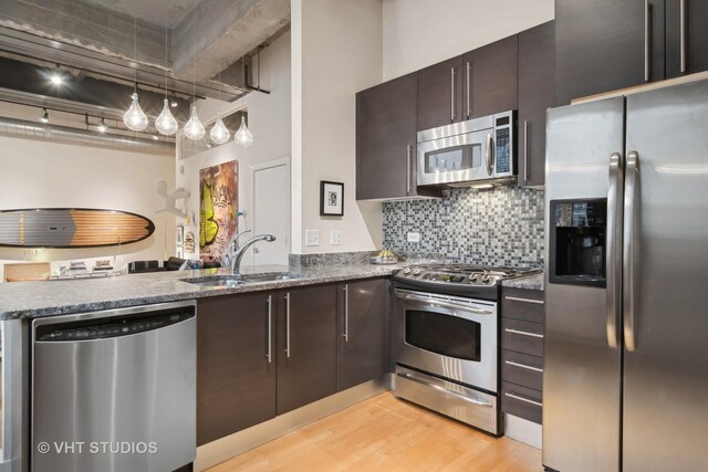 kitchen featuring stone counters, stainless steel appliances, backsplash, light wood-style flooring, and a sink