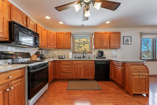 kitchen with light wood-style flooring, a peninsula, a sink, black appliances, and brown cabinetry