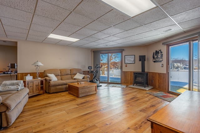 living area with a paneled ceiling, a wood stove, wainscoting, and light wood finished floors