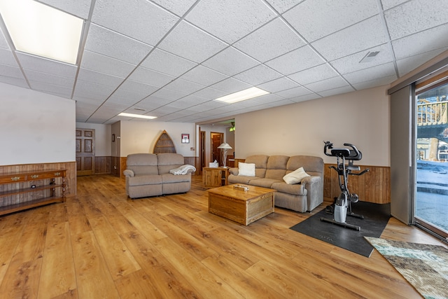 living area featuring a drop ceiling, wood walls, wainscoting, and wood finished floors